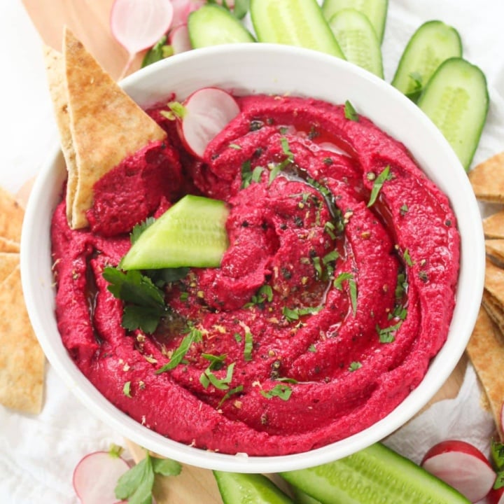 Beetroot hummus in a bowl with pickles and pita bread