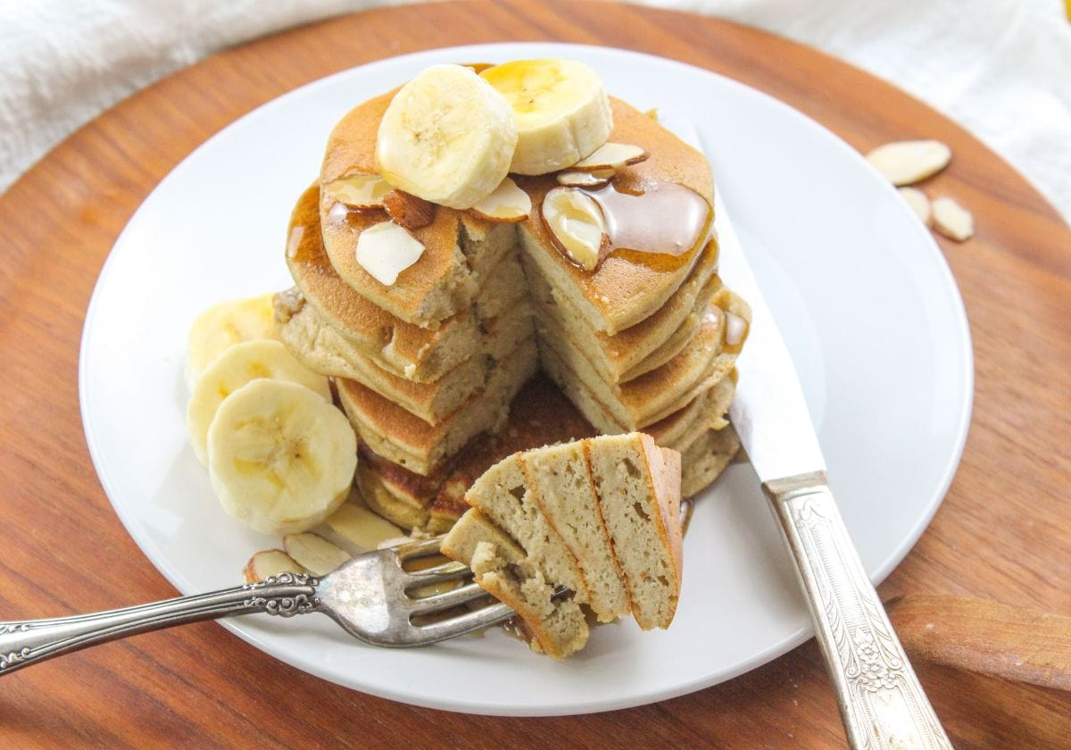 stack of almond flour banana pancakes with banana slices and maple syrup with a fork