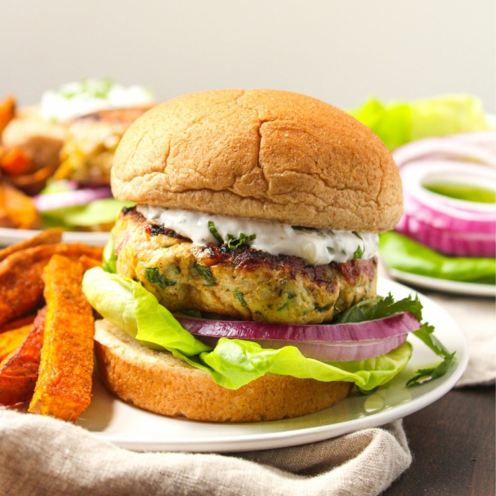 curry turkey burgers with yogurt sauce on a white plate with sweet potato fries