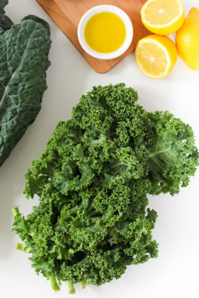 a bunch of kale next to sliced lemons and a small bowl of olive oil