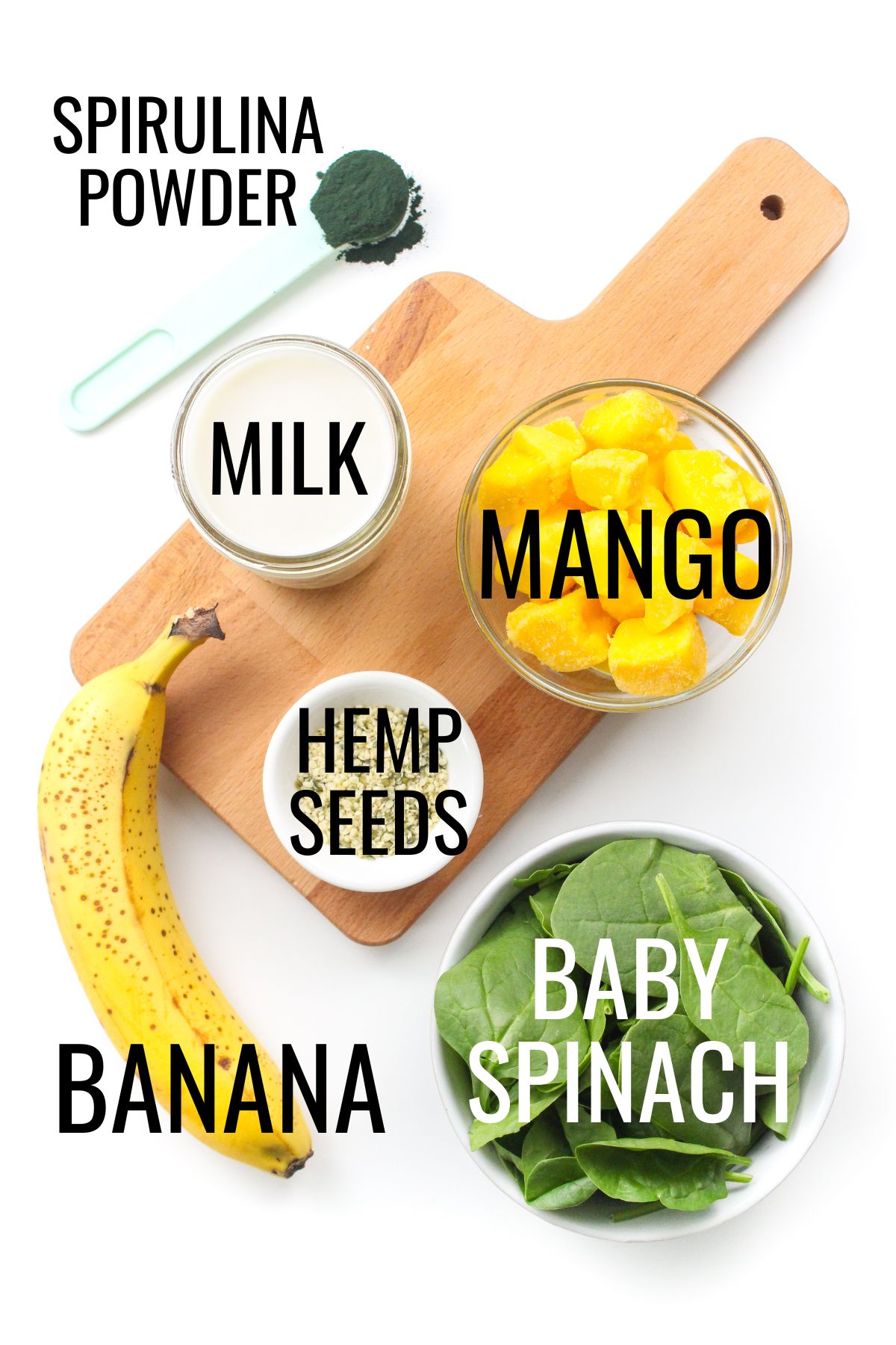 banana, spinach, mango, spirulina powder, hemp seeds, and milk in small bowls on a wooden board