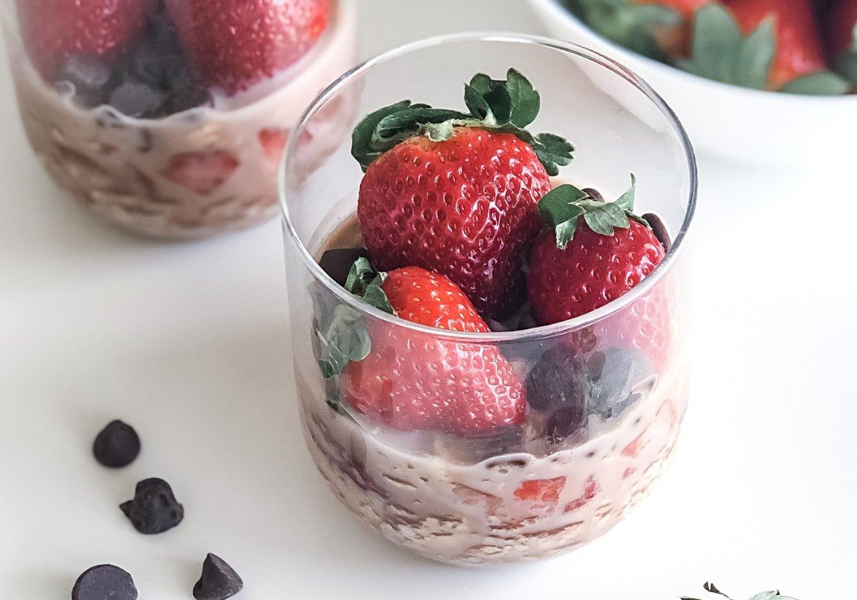chocolate strawberry overnight oats in jars with a bowl of strawberries in the background