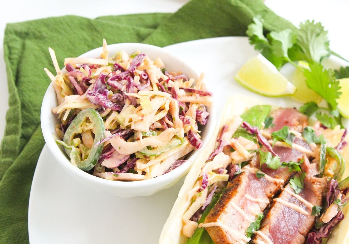 jalapeno slaw in a small bowl next to a fish taco on a plate