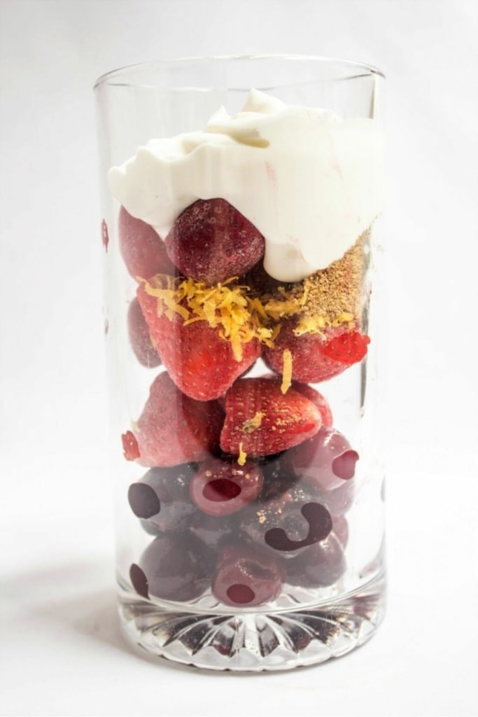 frozen strawberries, cherries, lemon zest, and greek yogurt in a tall glass