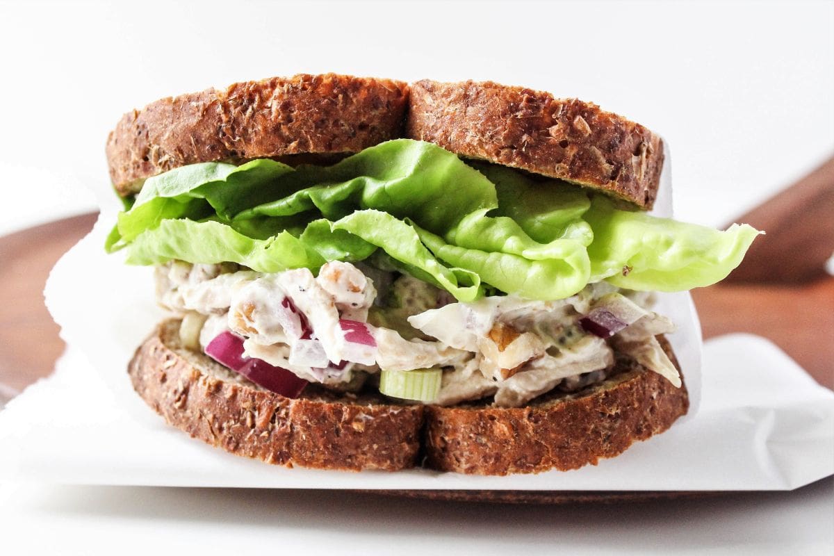 shredded chicken salad sandwich on a wooden platter with parchment paper