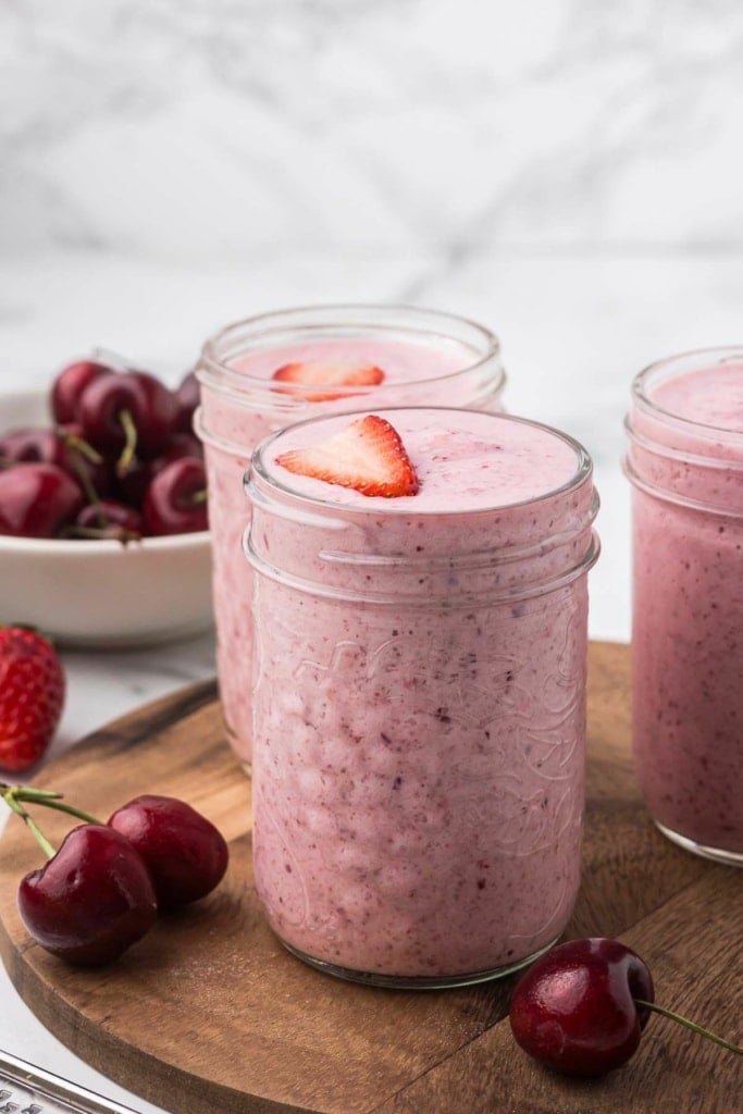 pink fruit smoothie on a wooden platter with strawberries and cherries