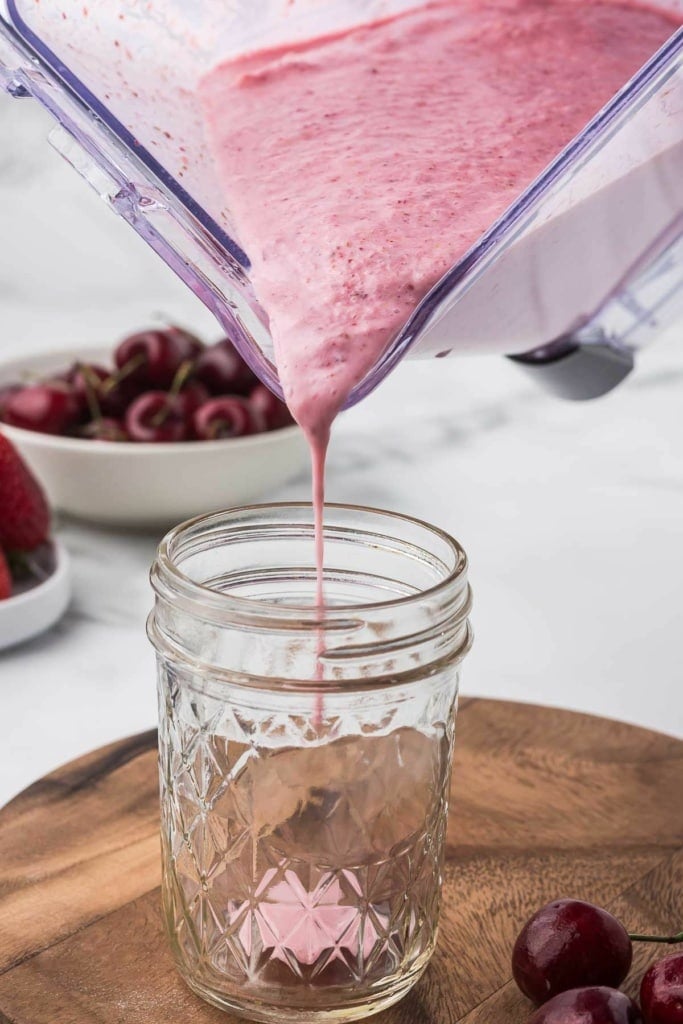 a pink smoothie being poured into a tall glass