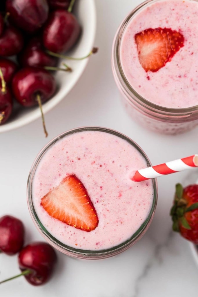 a strawberry cherry smoothie with a sliced strawberry and a striped straw in it