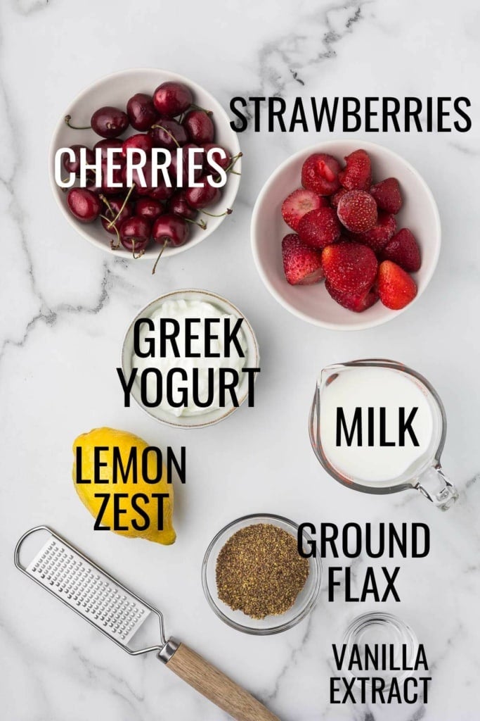 strawberries, cherries, Greek yogurt, milk, lemon, ground flax seed, and vanilla extract in small bowl on a marble countertop