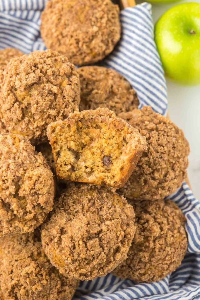 stack of apple muffins with crumble topping on a striped blue kitchen towel