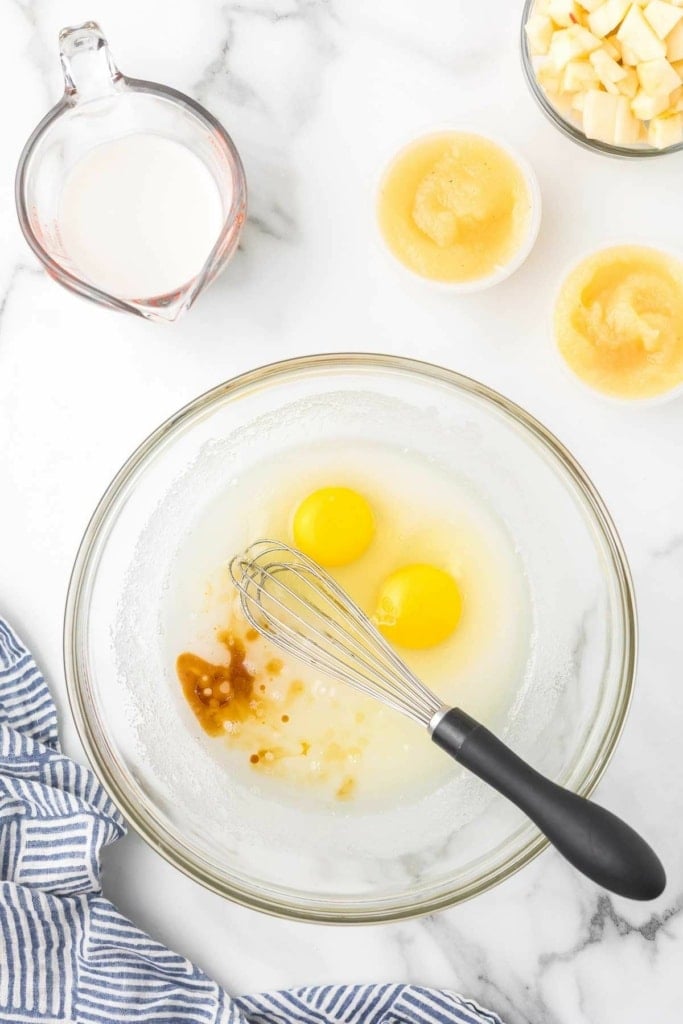 eggs, almond milk, applesauce, and vanilla extract in a glass bowl with a whisk