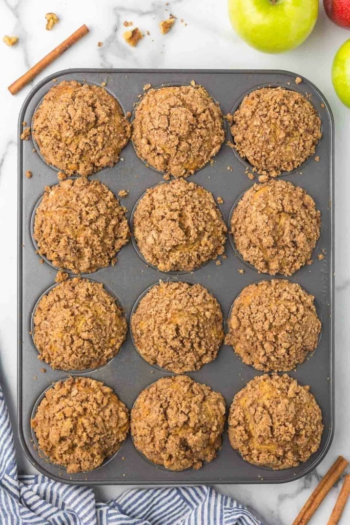 baked apple cinnamon muffins with crumb topping in a muffin tin