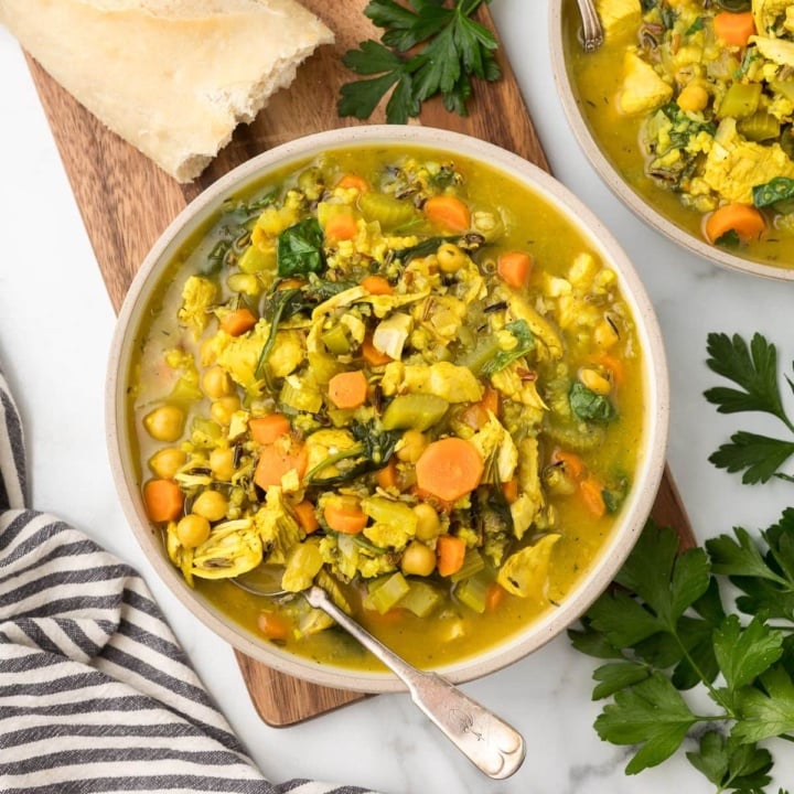 turkey rice soup in a bowl with a baguette next to it