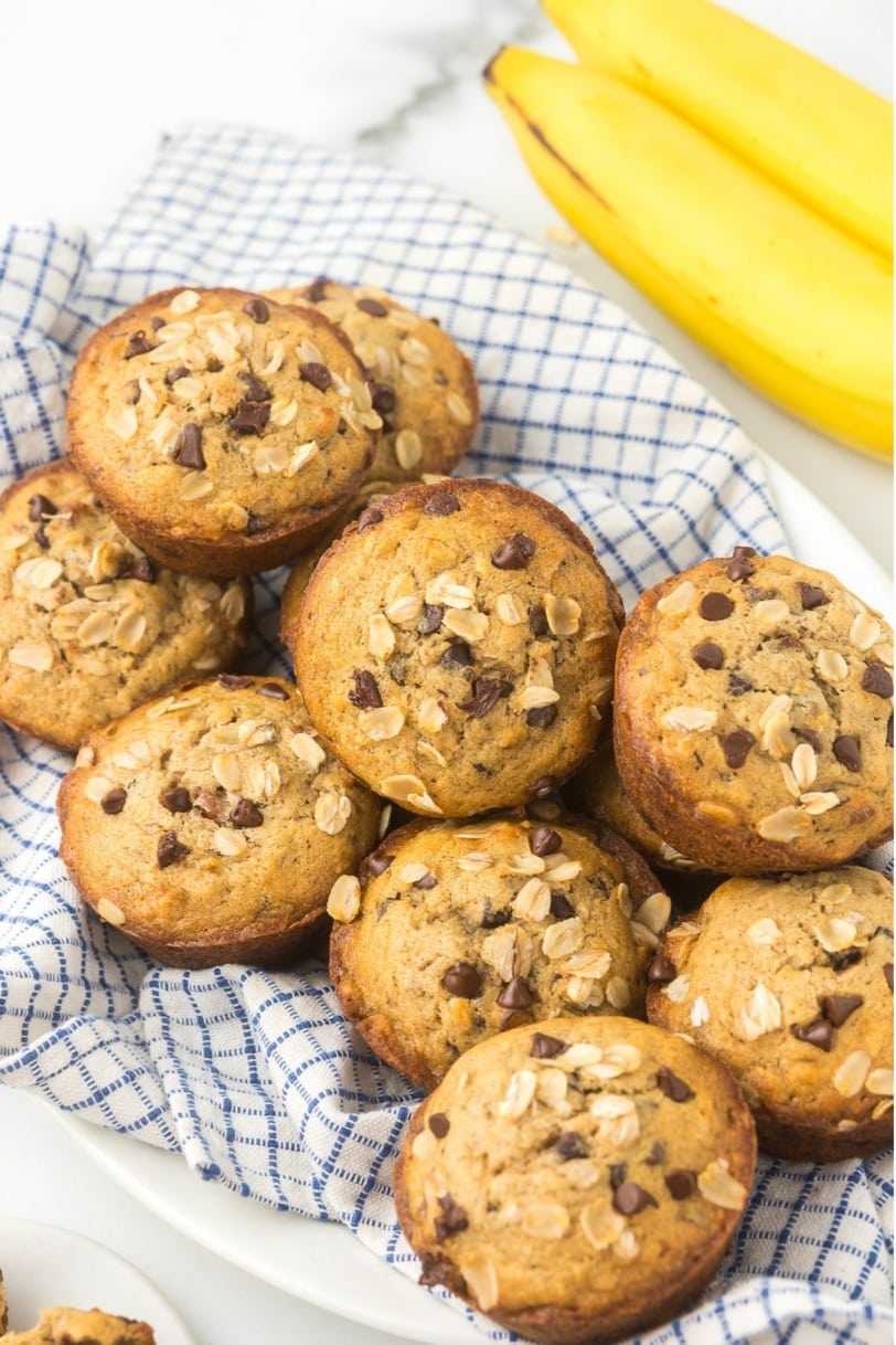 pile of gluten free banana nut muffins with chocolate chips on a striped kitchen towel