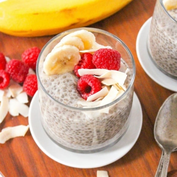 chia seed pudding with raspberries, coconut, and banana slices in a small glass jar