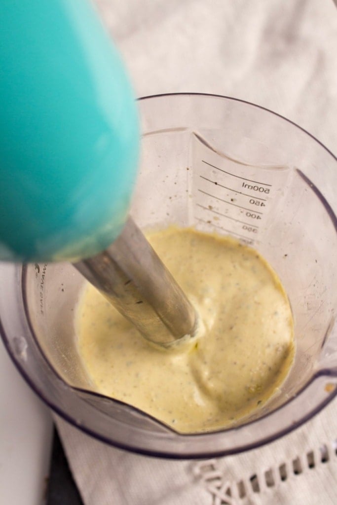blended vegan caesar salad dressing in a measuring cup with an immersion blender
