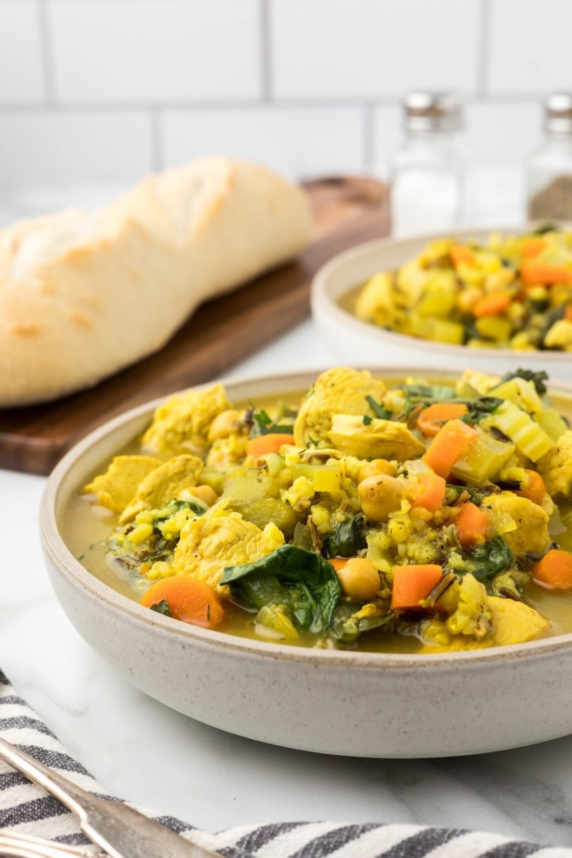 turkey rice soup with carrots in a bowl with a baguette next to it