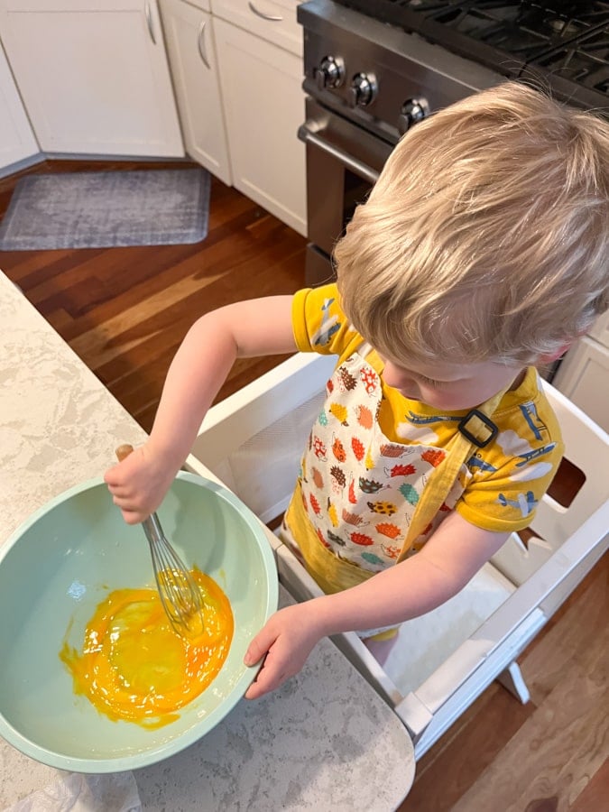 toddler whisking eggs in a bowl.