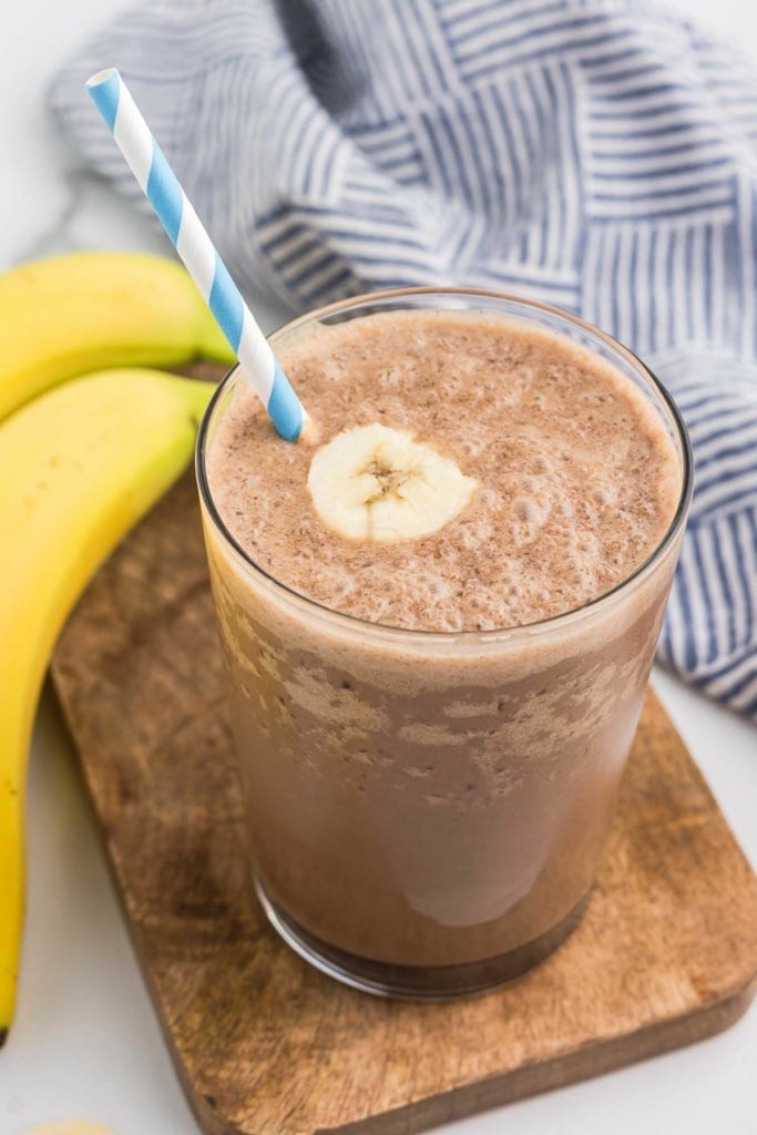 chocolate banana smoothie with peanut butter in a glass with a striped straw sitting on a wooden tray