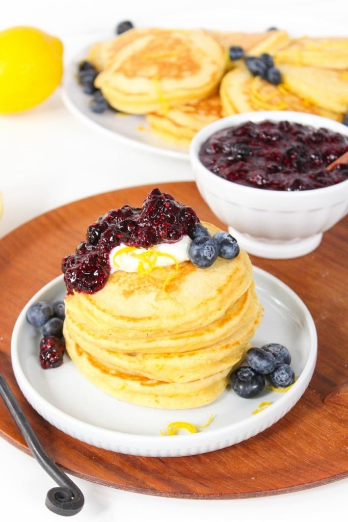 a bowl of blueberry chia jam next to a stack of lemon pancakes on a white plate