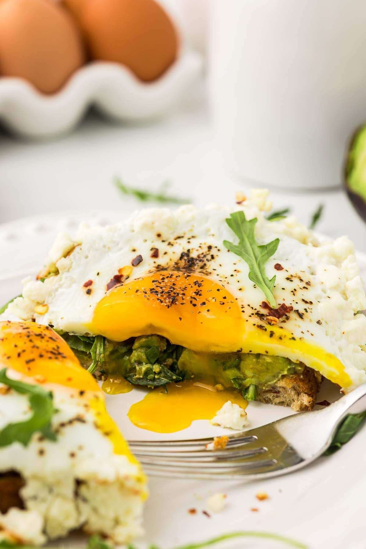 a fried egg with feta cheese cut in half on top of avocado toast