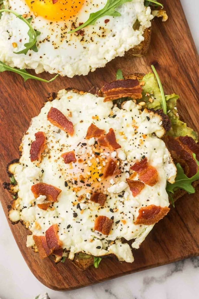 crispy feta eggs with bacon pieces on top sitting on a wooden platter