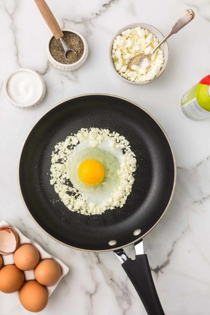 feta cheese with an egg cracked on top on a skillet