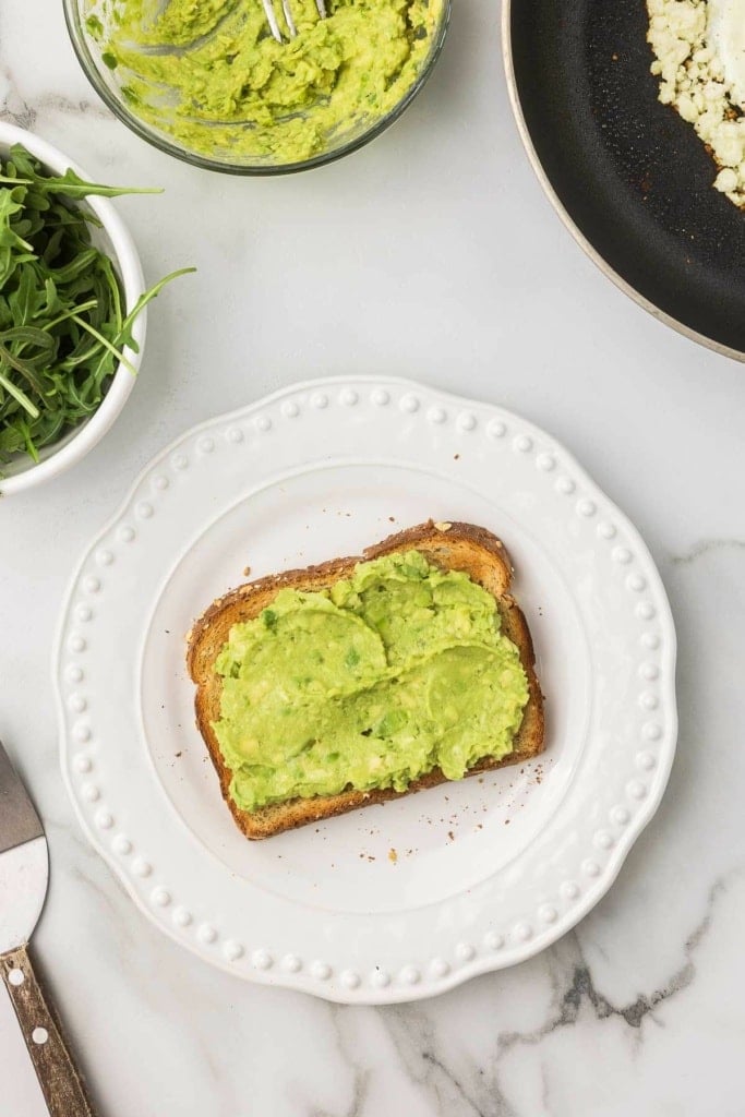 mashed avocado on a slice of toast on a white plate