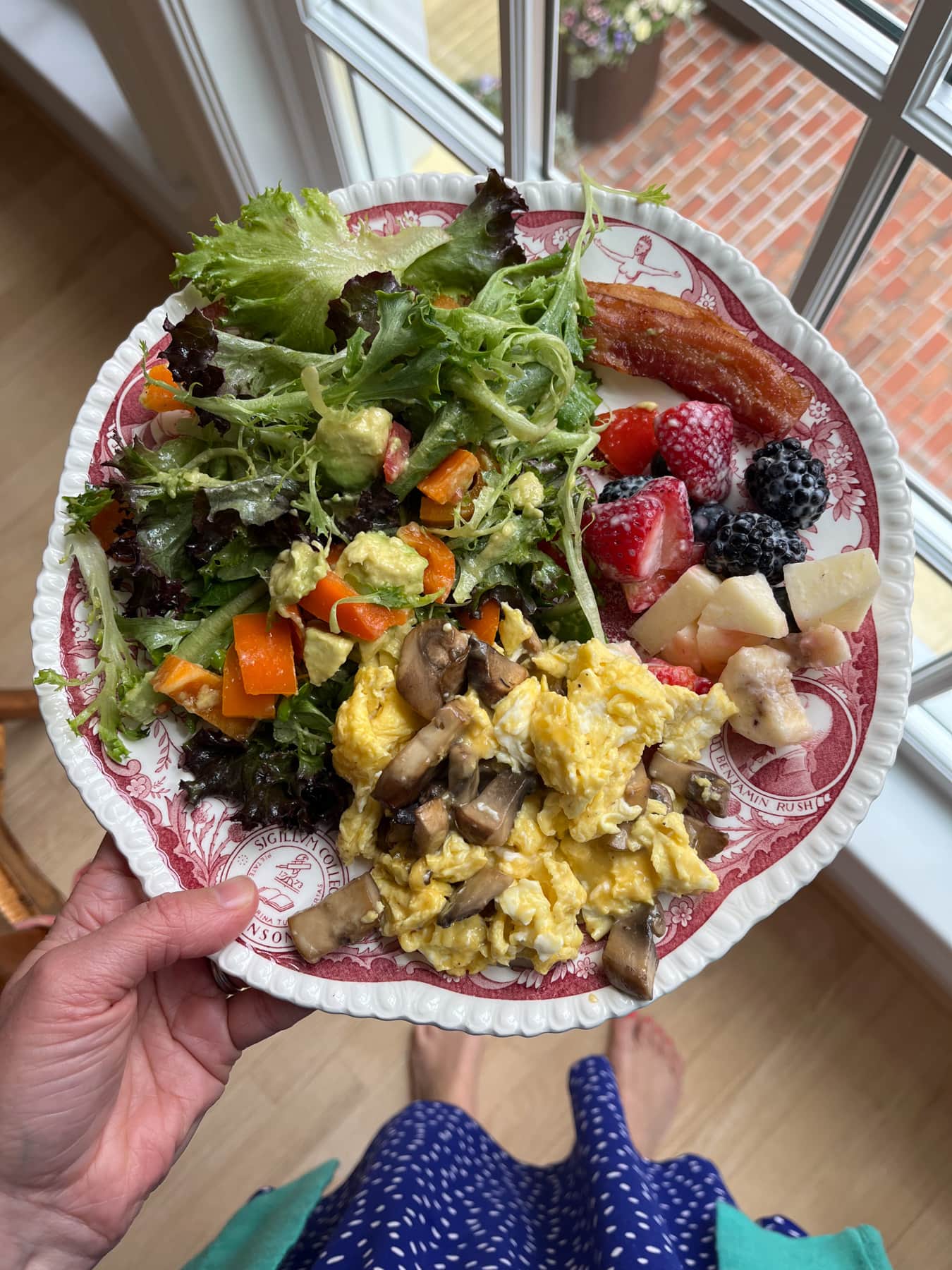 brunch plate filled with fruit, salad, eggs, and bacon