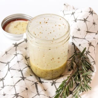 maple dijon dressing with apple cider vinegar in a mason jar with a sprig of rosemary beside it