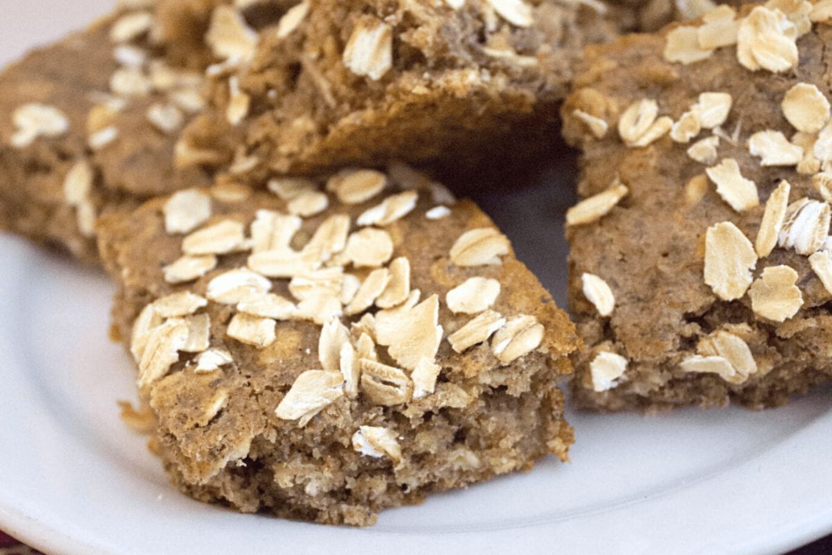 A stack of banana applesauce breakfast bars topped with oats on a white plate.
